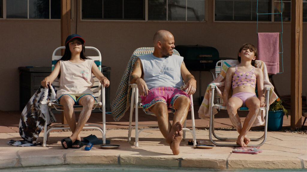 Three people sit in sunshine in folding lawn chairs