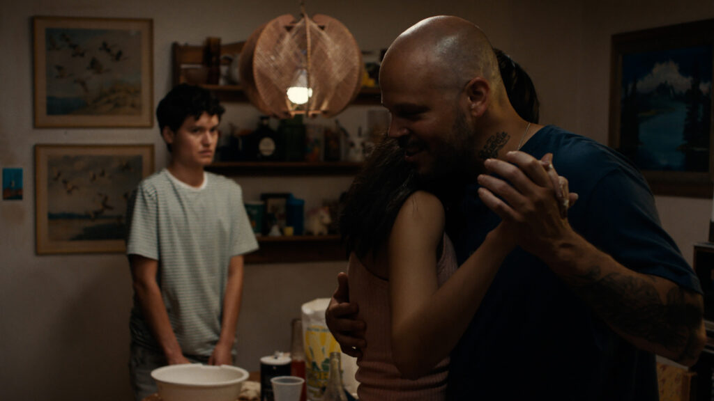 In low light room two people dance while one person watches