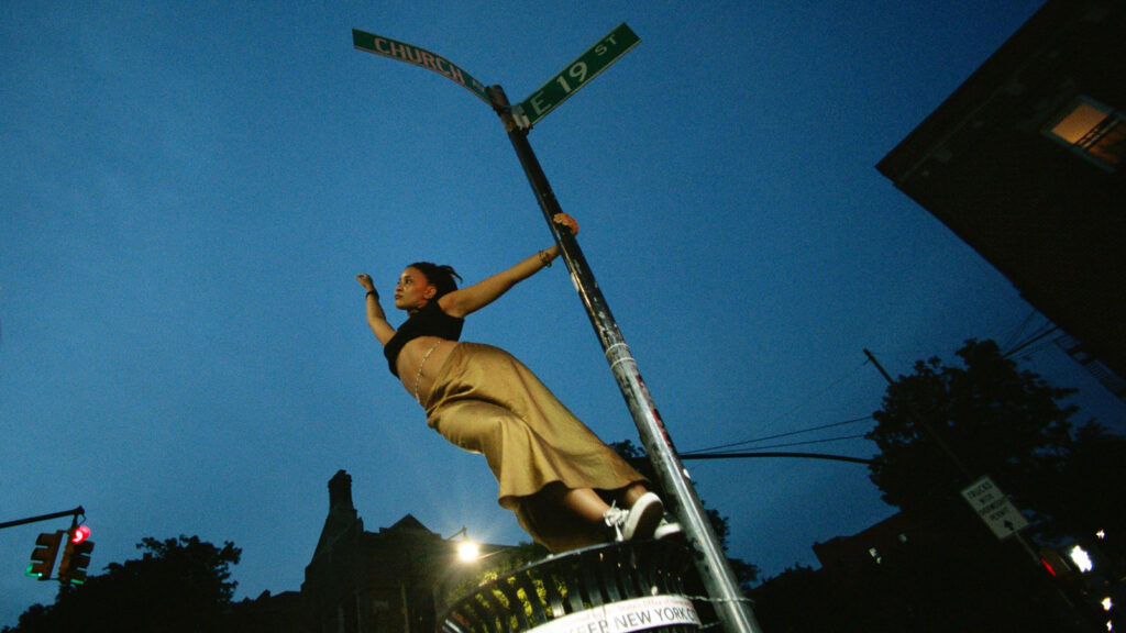 At night, person holds onto lamppost with one hand and other hand outstretched 