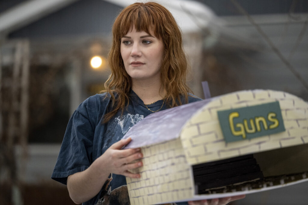 Person holding a model of a building that says "GUNS" on the front