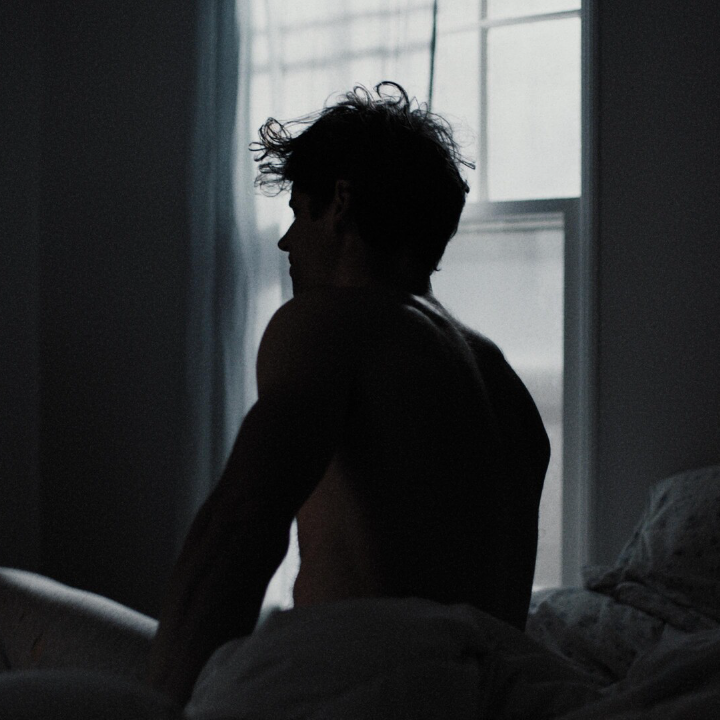 Person sits on bed with light from window